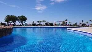 A clear blue pool with a rocky edge, surrounded by palm trees and umbrellas. - La Perla - South Facing, Sun Morning to Evening (Nerja)