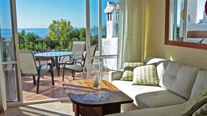 A room with a balcony, a sofa, a table, and a chair. - La Perla - South Facing, Sun Morning to Evening (Nerja)