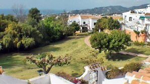A residential area with white buildings, a grassy lawn, and a tree in the foreground. - La Perla - South Facing, Sun Morning to Evening (Nerja)