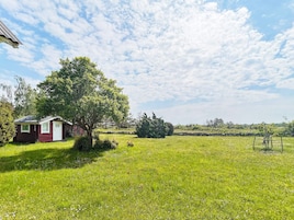A rural property with a small red building, a large tree, and a grassy field.