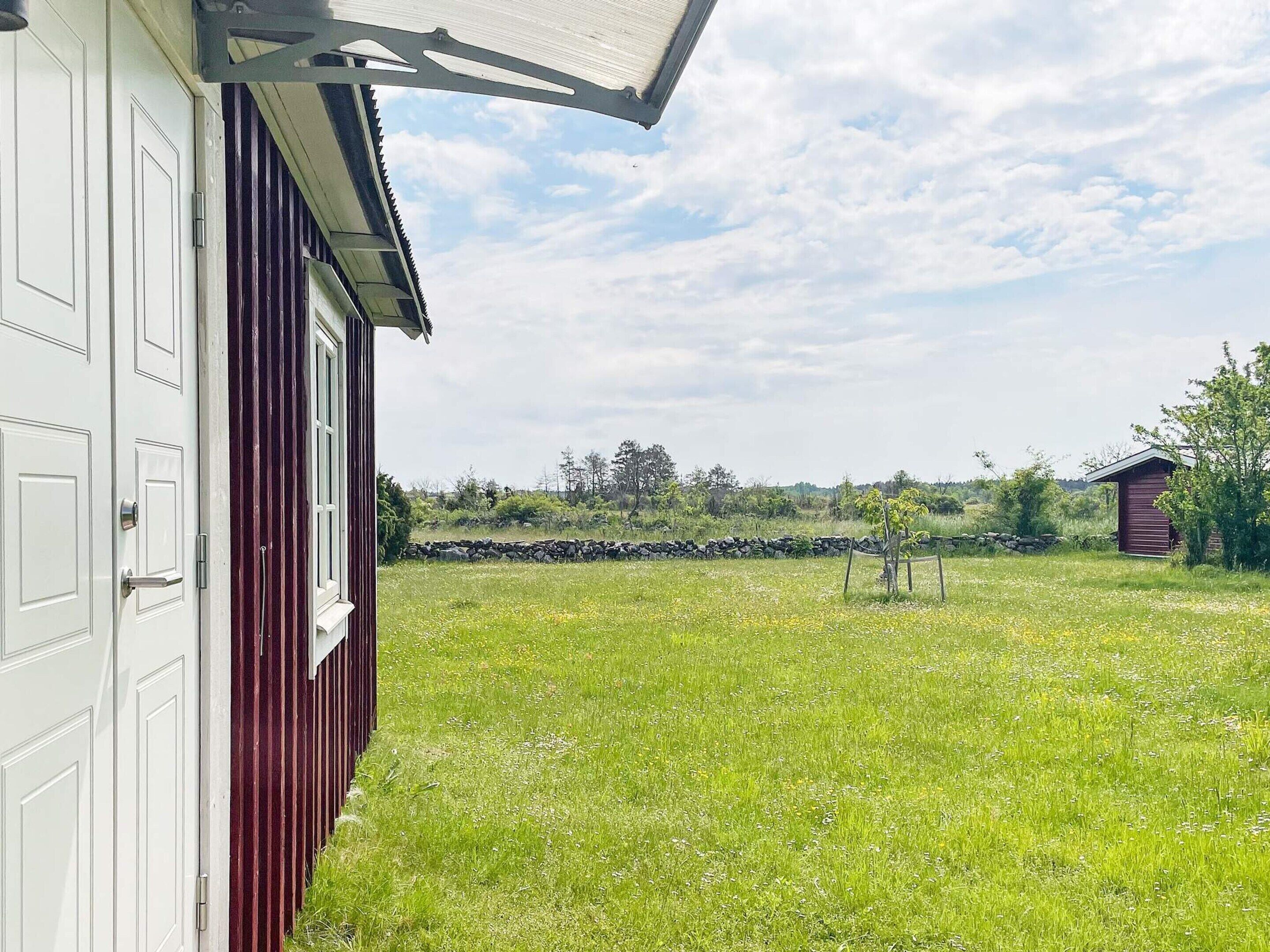 A red barn with a white door, a grassy field, and a stone wall in the background.