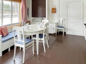 Un comedor con una mesa y sillas blancas, un banco con cojines, un reloj en la pared y una puerta.