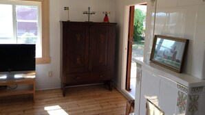 Ein Zimmer mit einem Holzkabinett, einem Fernseher auf einem Standfuß und einem Kamin mit einem Bilderrahmen darüber.