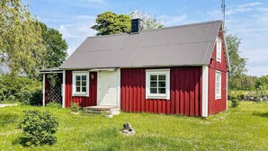Ein rotes Holzhaus mit weißer Tür, zwei Fenstern und einem Schornstein.