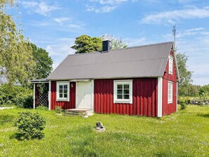 Una casa de madera roja con puerta blanca, dos ventanas y una chimenea.