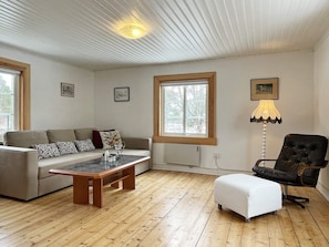 A living room with a sofa, a coffee table, a chair, and a window with a view of trees.
