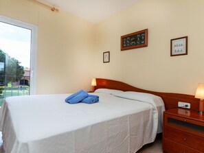 A hotel room with a bed, a nightstand, and a window with a view of a garden.