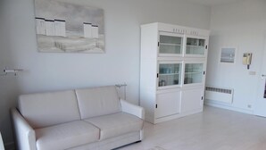 En minimalistisk stue med en hvid sofa, et skab med glaslåger og et billede på væggen.