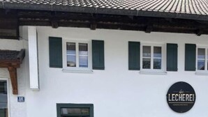 Un edificio con un letrero que dice "LECHEREI" y un pequeño espacio al aire libre con dos mesas y sillas.