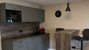 Una cocina moderna con armarios grises, encimera de madera y horno empotrado. Hay una mesa redonda con una silla, un reloj en la pared y una lámpara colgante.