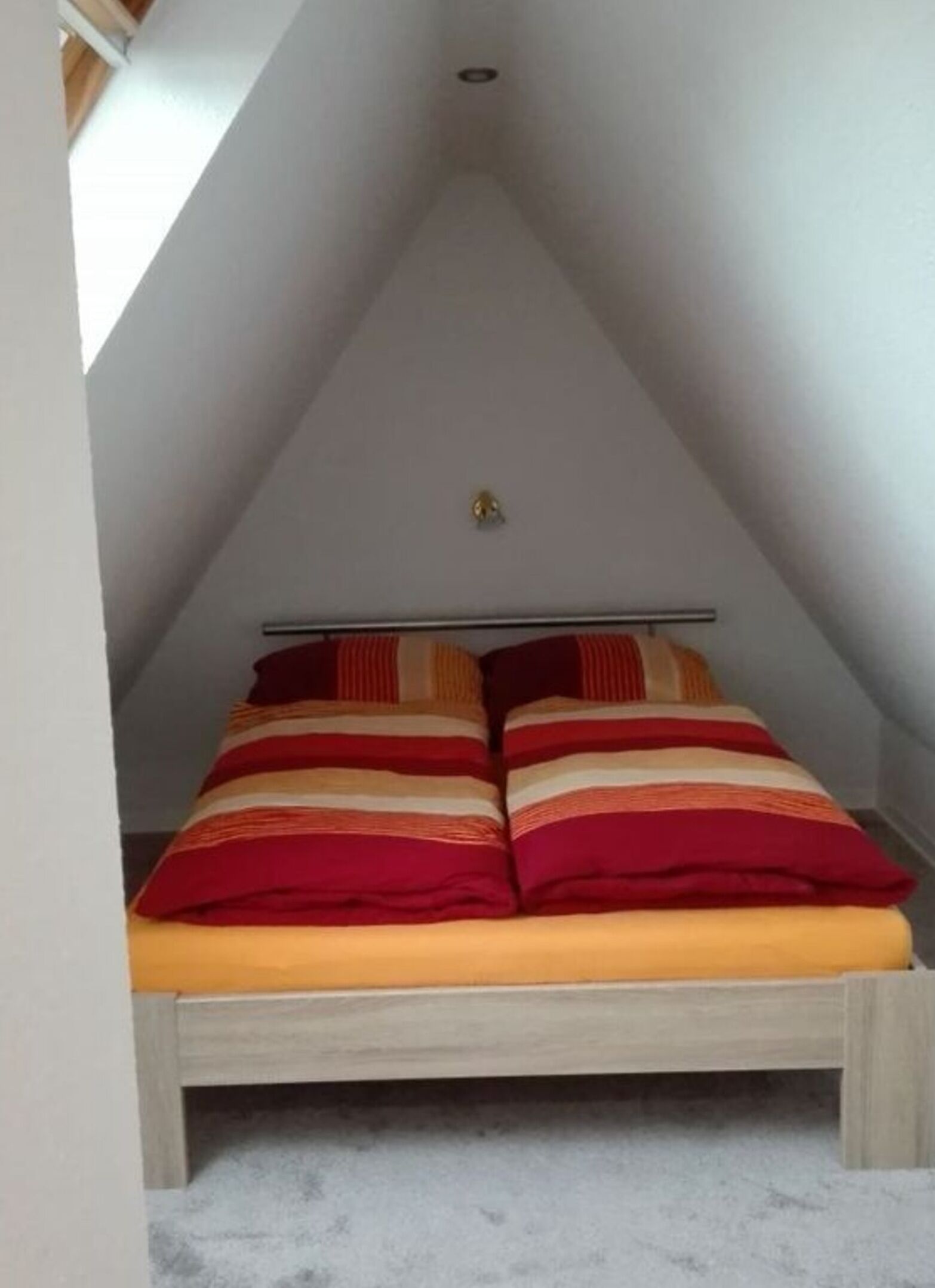 A bedroom with a sloped ceiling, a bed with striped bedding, and a visible light fixture.