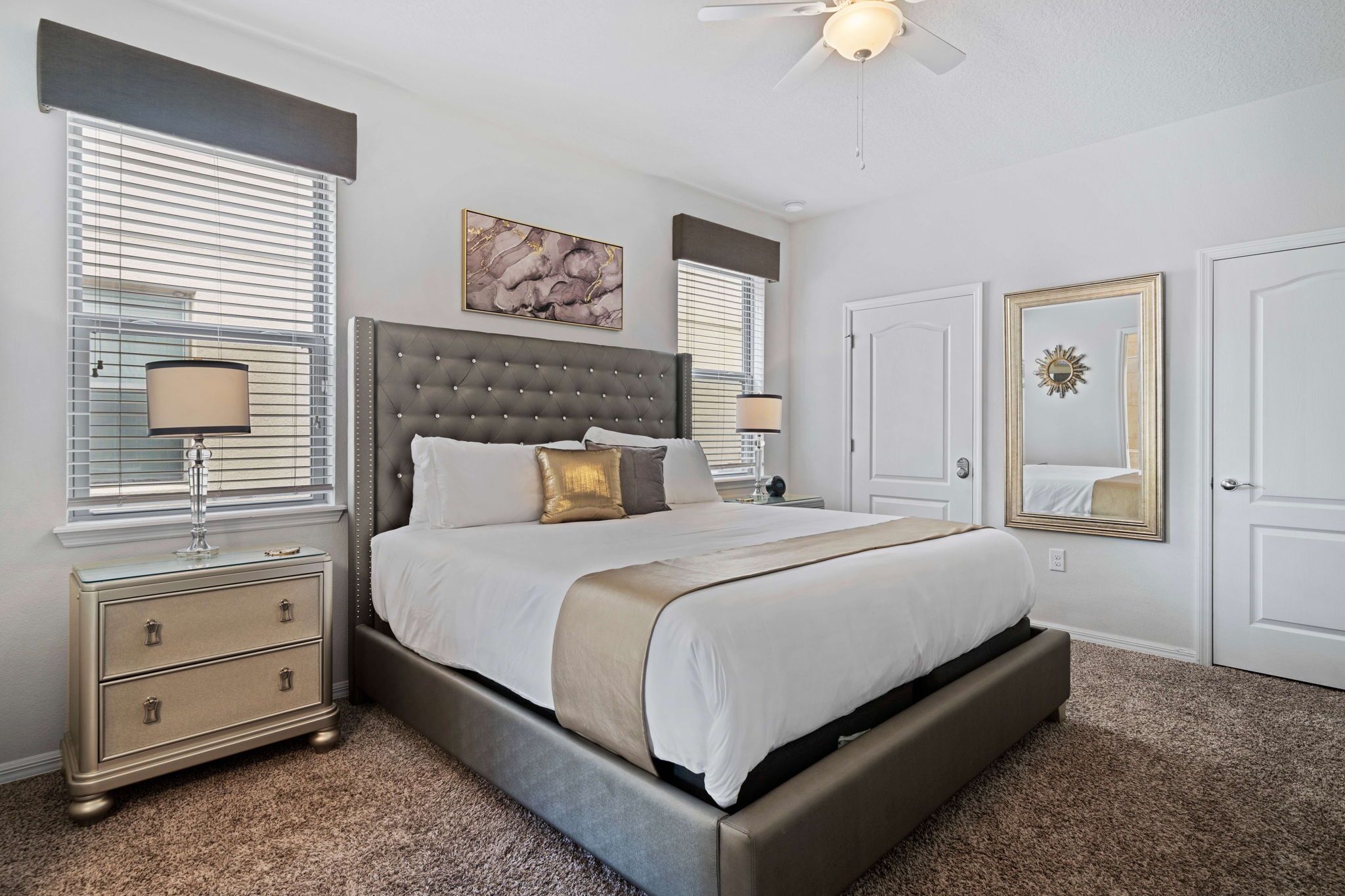 A bedroom with a large bed, two bedside tables, a ceiling fan, and a wall-mounted mirror.