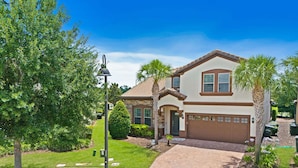 A two-story house with a brick driveway, a garage, and a well-maintained lawn.