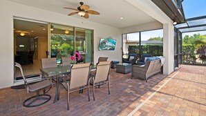 An outdoor patio with a glass door leading to a dining area, wicker furniture, and a ceiling fan.