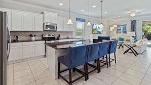 A modern kitchen with white cabinets, a central island with blue bar stools, and pendant lighting.