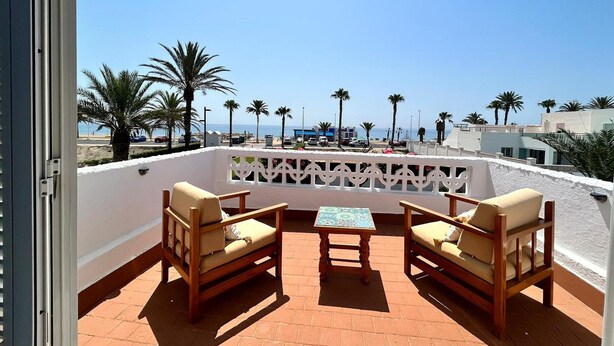 A terrace with two wooden chairs and a small table, overlooking a beach with palm trees and a clear sky. - Belvilla by OYO Casa Manuela (Roquetas de Mar)