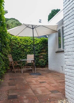 A patio with a table and chairs, a large umbrella, and a brick wall.