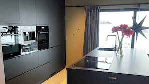 Een moderne keuken met inbouwapparatuur, een groot kookeiland met een spoelbak en een stersieradenering op de vensterbank.