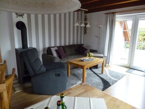 Ein Wohnzimmer mit einer Couch, einem Holztisch, einem Kamin und einer Schiebetür zum Garten.