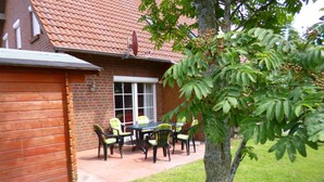 A patio with a table and chairs, a brick wall, and a tree. - Holiday Home Christmann (Wangerland)