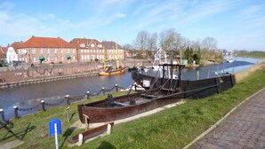 A riverside view with a historic boat on display, a brick pathway, and traditional buildings in the background. - Holiday Home Christmann (Wangerland)