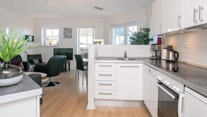 Een moderne keuken met witte kasten, een roestvrijstalen afzuigkap en een ingebouwde oven. Er is een eethoek met een zwarte stoel en een kleine tafel.