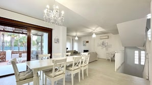 Un comedor espacioso con una mesa y sillas blancas, un candelabro y vistas al exterior.