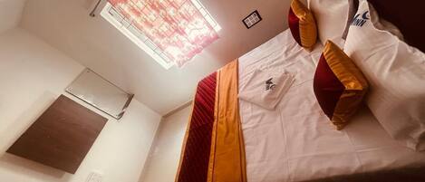A neatly made bed with a red and yellow bedspread, white pillows, and a window with a floral curtain.