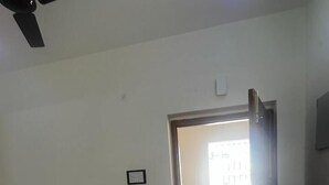 An empty room with a ceiling fan, a door leading to another room, and a light fixture on the ceiling.