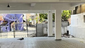 A spacious indoor area with a tiled floor, white pillars, and a view of a gated outdoor area.