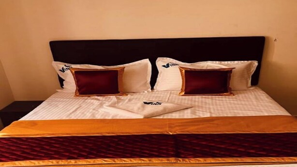 A neatly made bed with a striped white and gold bedspread, two red pillows, and a dark headboard.