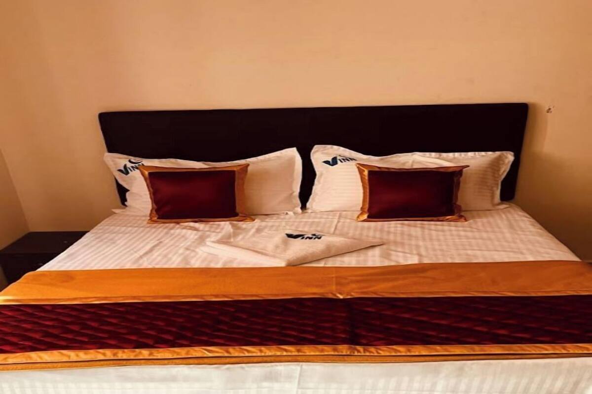 A neatly made bed with a striped white and gold bedspread, two red pillows, and a dark headboard.