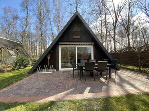 A modern, triangular wooden cabin with a patio area featuring a brick floor and outdoor furniture. - Holiday Home Seehutte (Malschwitz)
