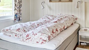 Una cama con colcha y almohadas estampadas, una mesita de noche con lámpara y una ventana con cortinas.