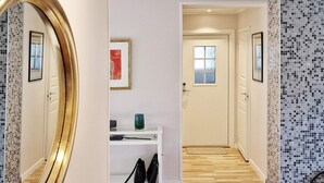 Un pasillo con una consola blanca, un espejo y una puerta que da a otra habitación.