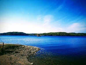 Un lac paisible, avec une petite barque et une île boisée qui se dessine à l’horizon.