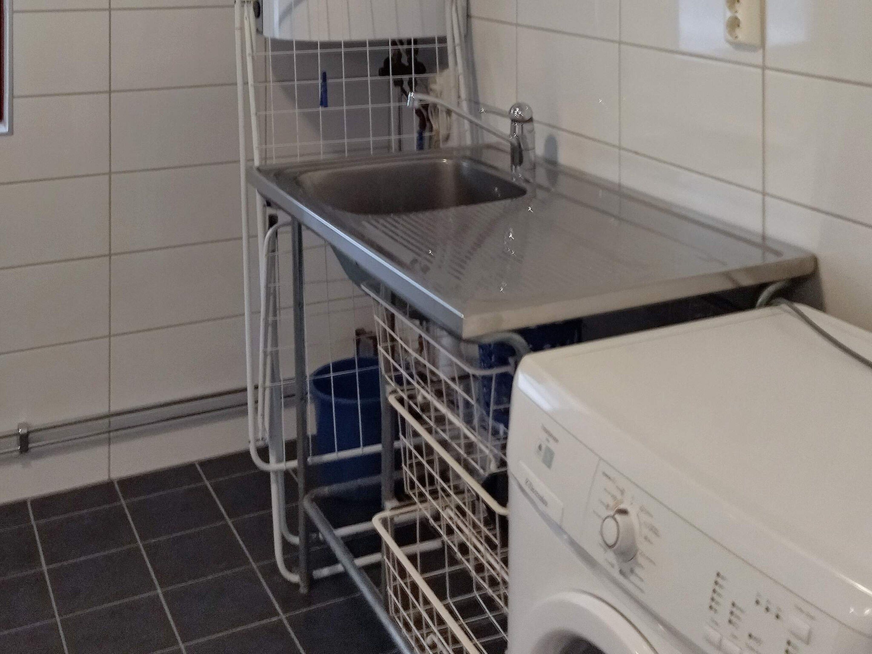 A laundry area with a washing machine, a sink, and a metal rack.