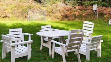 A set of white outdoor furniture consisting of a round table and six chairs arranged on a grassy lawn.