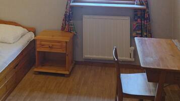 A small room with a bed, a wooden nightstand, a table, and a chair.