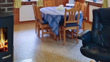 A dining area with a table set for four, surrounded by wooden chairs. A black leather chair is positioned to the right.