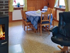 A dining area with a table set for four, surrounded by wooden chairs. A black leather chair is positioned to the right. - 6 Person Holiday Home in Ed (Ed)