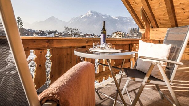 A wooden balcony with a table, a bottle, and glasses, overlooking a snowy mountain landscape. - Chalet in Reith Near Ski Juwel Alpbachtal (Reith im Alpbachtal)
