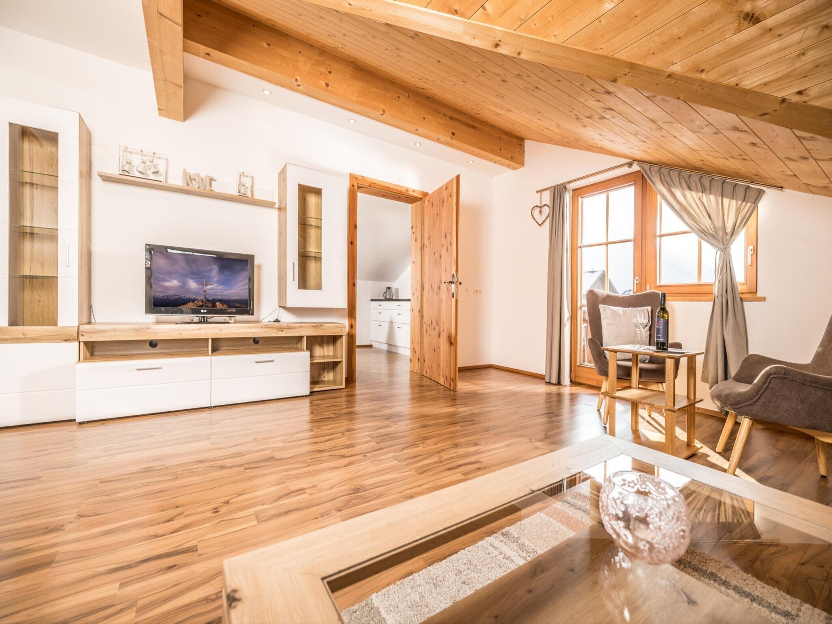 Ein modernes Wohnzimmer mit Holzboden, einem Fernseher, einem Sofa und einem Essbereich.