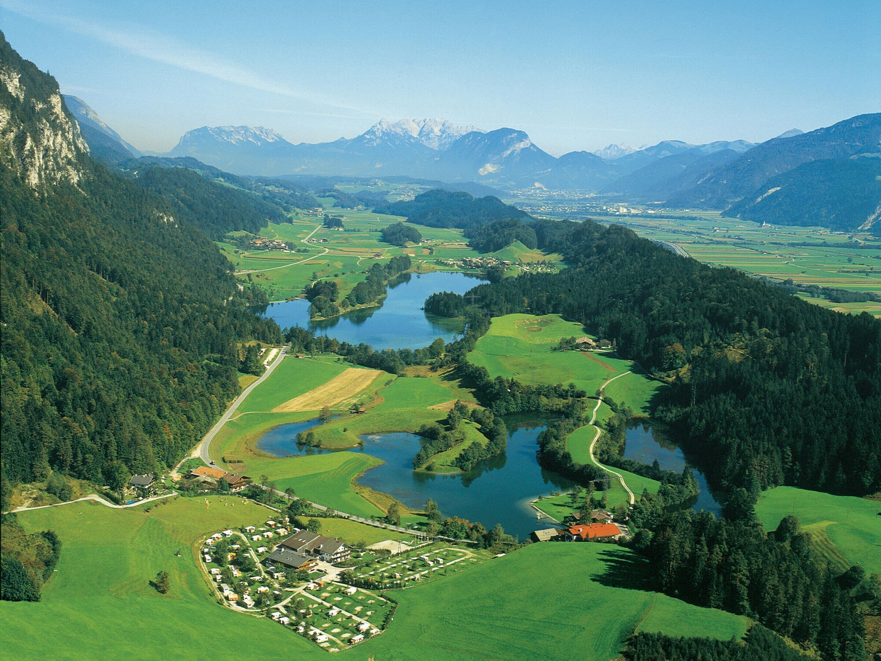 Un paisaje montañoso con un lago, campos verdes y un pequeño pueblo con edificios y caminos.
