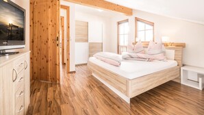 A bedroom with a wooden ceiling, a bed with multiple pillows, a TV on a wooden cabinet, and a wooden floor. - Chalet in Reith Near Ski Juwel Alpbachtal (Reith im Alpbachtal)