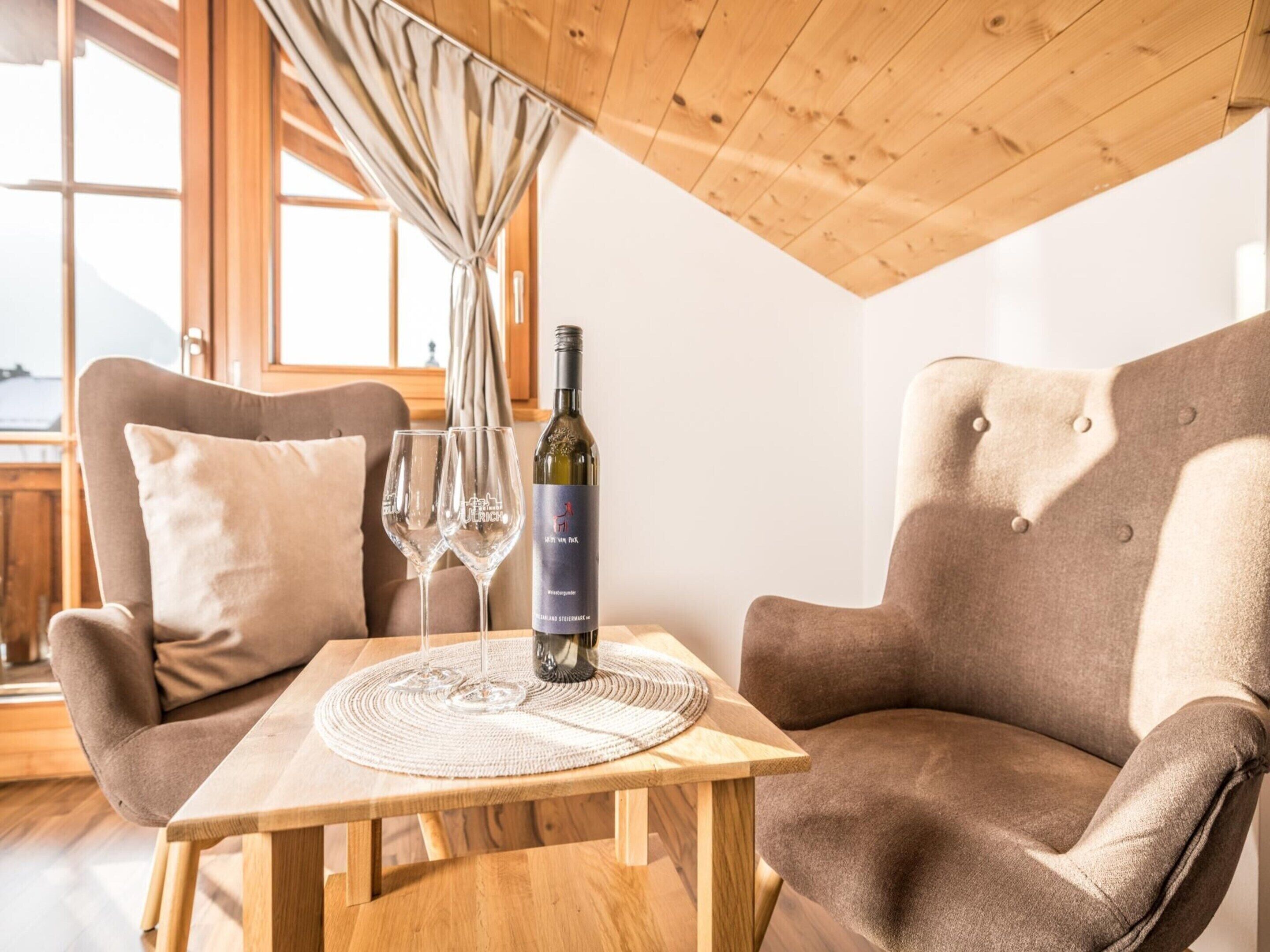 Une pièce chaleureuse avec deux fauteuils marron, une table en bois et une bouteille de vin posée sur un set de table.