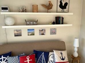 A living room with a beige sofa, nautical-themed pillows, and a white lamp.