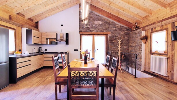 A wooden interior with a dining table, chairs, a kitchen area, and a stone wall. - Belvilla by OYO Pleasant Holiday Home With Garden (Lozzo di Cadore)
