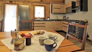 A wooden interior with a kitchen area, including a table with cups and a coffee pot, and a window with curtains. - Belvilla by OYO Pleasant Holiday Home With Garden (Lozzo di Cadore)