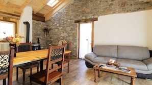 A cozy room with a stone wall, wooden ceiling, and a grey sofa. - Belvilla by OYO Pleasant Holiday Home With Garden (Lozzo di Cadore)